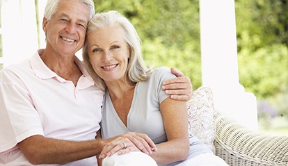 Older couple sitting and smiling with dentures