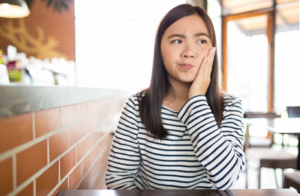 Young woman holding her jaw in concern because her tooth feels loose